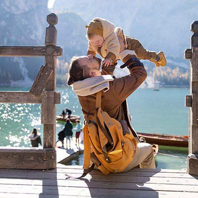 Father sitting on a dock near a lake lifts his infant in the air