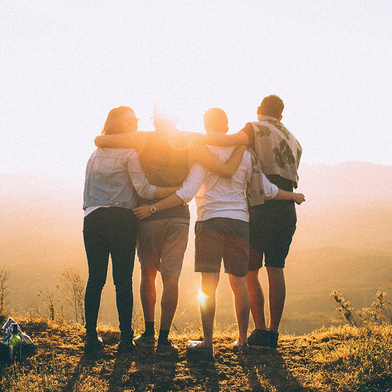 Four People Standing on Cliff in Front of Sun